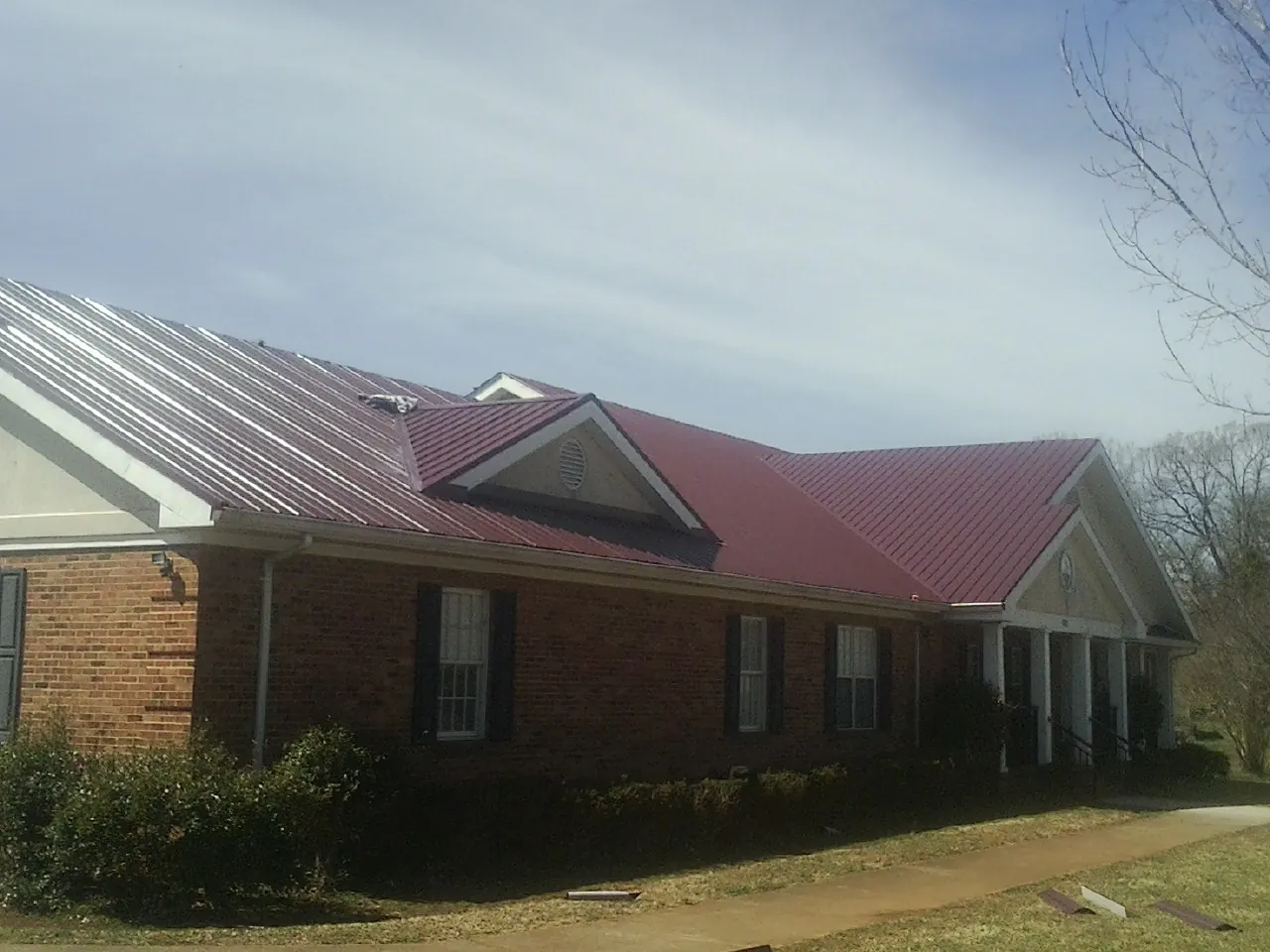 Red metal roof with gabled entries on a long brick building, from a Hail Damage Roof Repair job in Nome