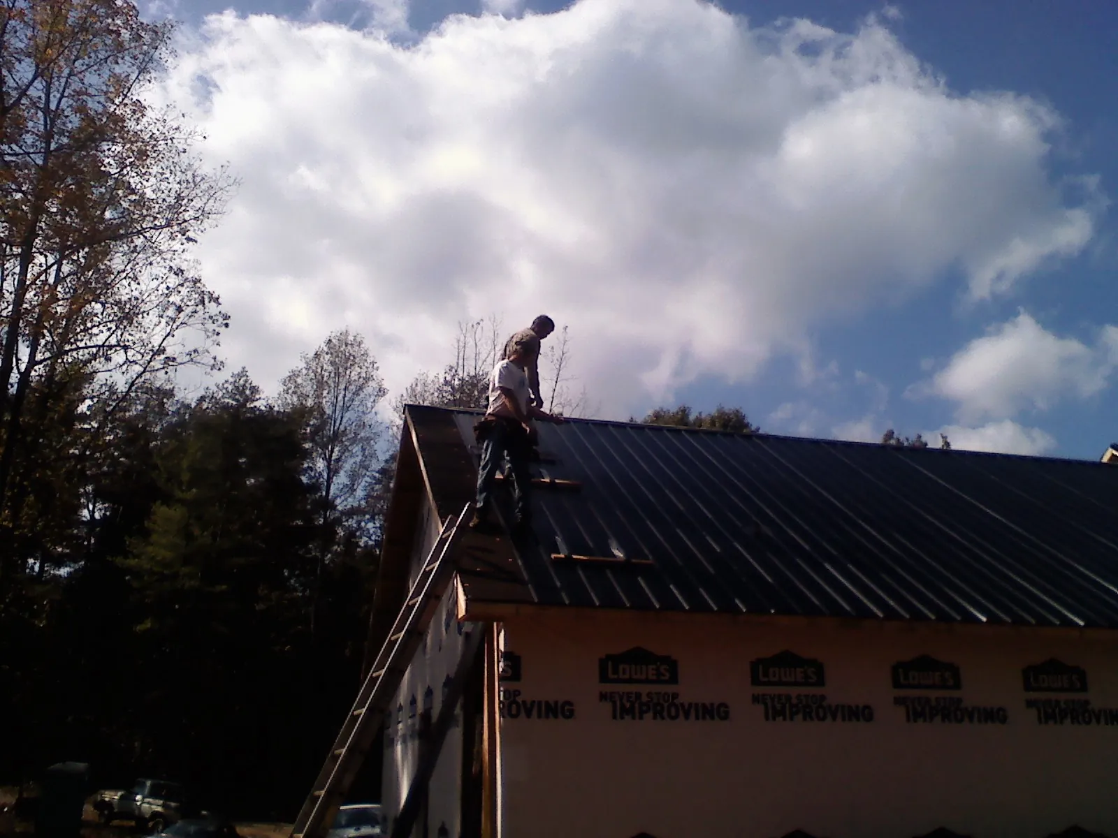 Roofer fastening dark metal panels high against a cloudy sky, from a Roof Inspection job in Nome